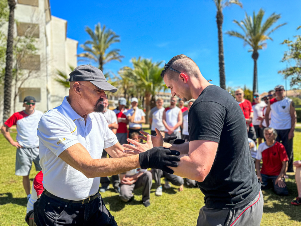 Professor Doktor Keith R. Kernspecht in einer Trainingssituation mit einem Schüler, während andere Schüler im Hintergrund zu sehen sind.